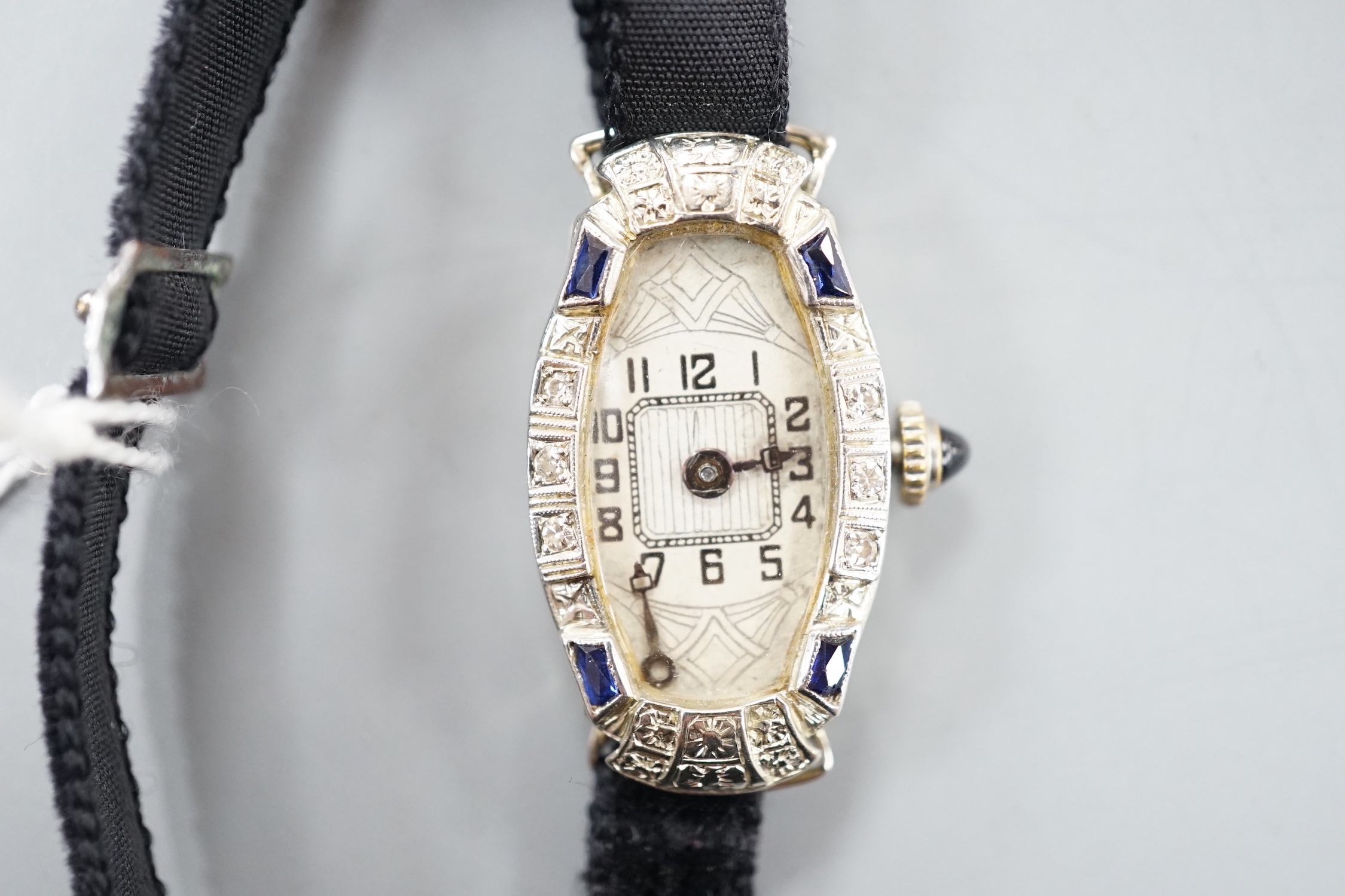 A lady's 18k white metal sapphire and diamond set manual wind cocktail watch, on fabric strap, gross weight 11.7 grams.